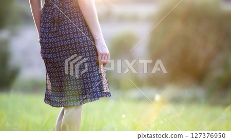 Young woman standing alone on a field with green grass enjoying warm sunset. Young woman standing alone on a field with green grass enjoying warm sunset. 127376950