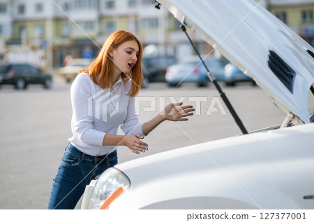 Young stressed woman driver standing near broked car with open hood. Young stressed woman driver standing near broked car with open hood. 127377001