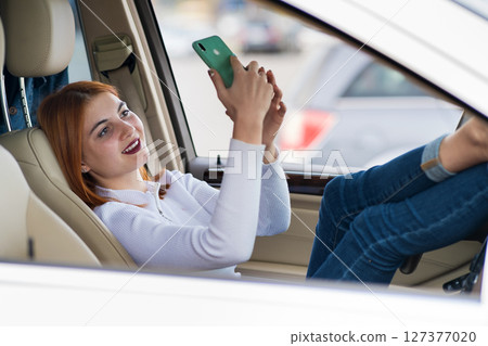 Young redhead woman driver taking selfies with her mobile phone sitting behind the wheel of the car in rush hour traffic jam. 127377020