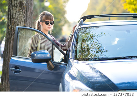 Young happy female driver standing near her car on a city street in summer. Travel destinations and transportation concept. Young happy female driver standing near her car on a city street in summer. Travel destinations and transportation concept. 127377038