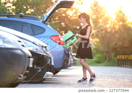 Young female driver putting luggage suitcase bag inside her car. Travelling and vacations concept Young female driver putting luggage suitcase bag inside her car. Travelling and vacations concept 127377044