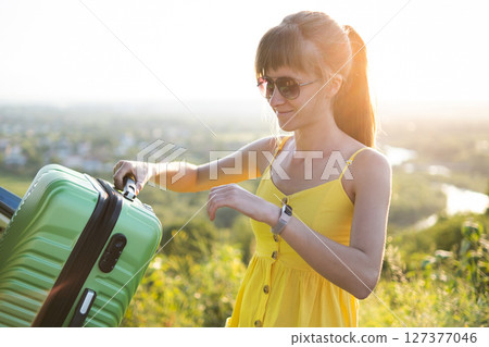 Young female driver putting green suitcase inside her car trunk. Travel and vacations concept. Young female driver putting green suitcase inside her car trunk. Travel and vacations concept. 127377046