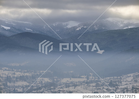 Winter landscape with mountain hills covered with evergreen pine forest after heavy snowfall on cold quiet evening Winter landscape with mountain hills covered with evergreen pine forest after heavy snowfall on cold quiet evening 127377075