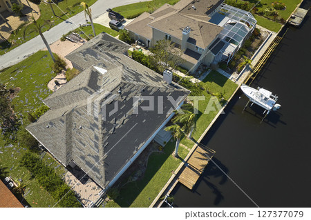 Wind damaged house roof with missing asphalt shingles after hurricane Ian in Florida. Repair of home rooftop concept Wind damaged house roof with missing asphalt shingles after hurricane Ian in Florida. Repair of home rooftop concept 127377079