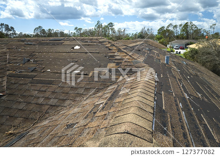Wind damaged house roof with missing asphalt shingles after hurricane Ian in Florida. Repair of home rooftop concept 127377082