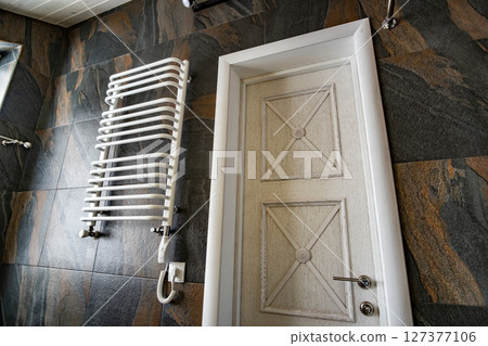 White contemporary electric towel dryer mounted on black tiled wall in modern bathroom. 127377106