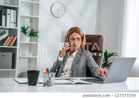 Talking by phone. Woman in business formal clothes is working in office Talking by phone. Woman in business formal clothes is working in office 127377209