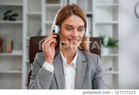 In the call center. In headphones. Woman in business formal clothes is working in office 127377225