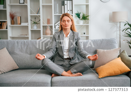 Lotus pose, meditation. Woman in formal clothes is at home, sitting on the sofa 127377313