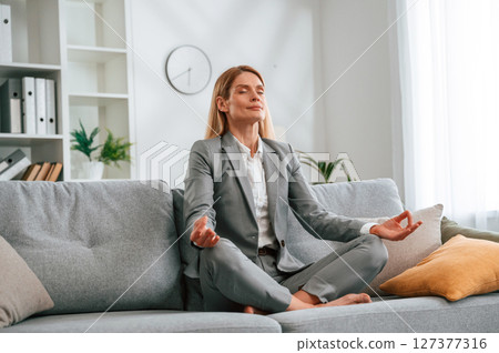 Lotus pose, meditation. Woman in formal clothes is at home, sitting on the sofa Lotus pose, meditation. Woman in formal clothes is at home, sitting on the sofa 127377316