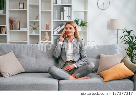 Having a call. Woman in formal clothes is at home, sitting on the sofa Having a call. Woman in formal clothes is at home, sitting on the sofa 127377317