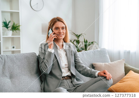 Having a call. Woman in formal clothes is at home, sitting on the sofa Having a call. Woman in formal clothes is at home, sitting on the sofa 127377318