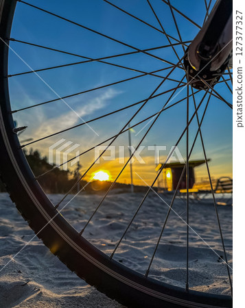 Bicycle wheel close-up on sandy beach at sunset, capturing evening light and tranquil atmosphere 127377327