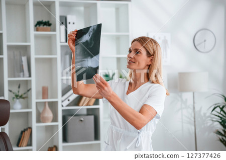 Checking x-ray. Young female doctor in white coat is indoors 127377426