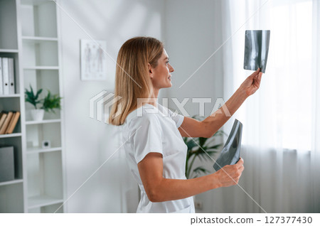 Checking x-ray. Young female doctor in white coat is indoors Checking x-ray. Young female doctor in white coat is indoors 127377430