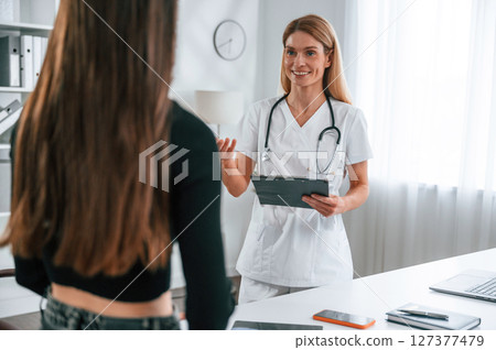 Standing, giving advice, holding notepad. Young woman at a nutritionist's appointment. Medical care Standing, giving advice, holding notepad. Young woman at a nutritionist's appointment. Medical care 127377479