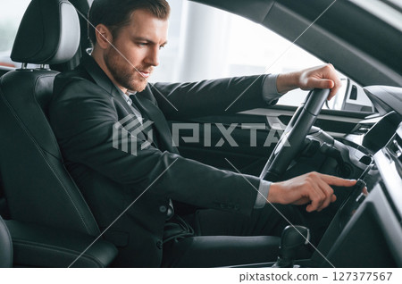 Turning the knobs. Man in formal business clothes is sitting in the modern automobile 127377567