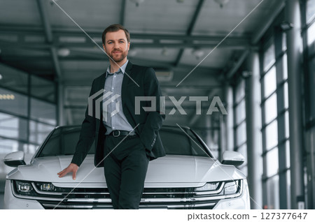 Man in black suit is indoors in the car dealership near automobile 127377647