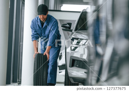 Moving the tire. Man in blue uniform is working in the car service 127377675