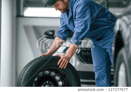 Moving the tire. Man in blue uniform is working in the car service Moving the tire. Man in blue uniform is working in the car service 127377677