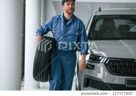 With tire in the hands. Man in blue uniform is working in the car service 127377687