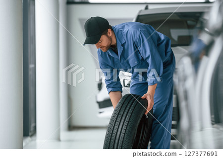 Tire replacement concept. Man in blue uniform is working in the car service Tire replacement concept. Man in blue uniform is working in the car service 127377691