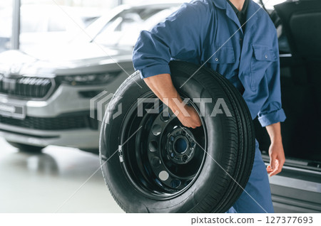 Tire replacement concept. Man in blue uniform is working in the car service Tire replacement concept. Man in blue uniform is working in the car service 127377693