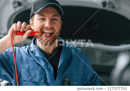 Red colored electrical terminal, Having fun, dangerous. Man in blue uniform is working in the car service Red colored electrical terminal, Having fun, dangerous. Man in blue uniform is working in the car service 127377703