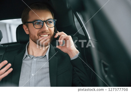 Talking by phone. Man in formal business clothes is sitting in the modern automobile Talking by phone. Man in formal business clothes is sitting in the modern automobile 127377708