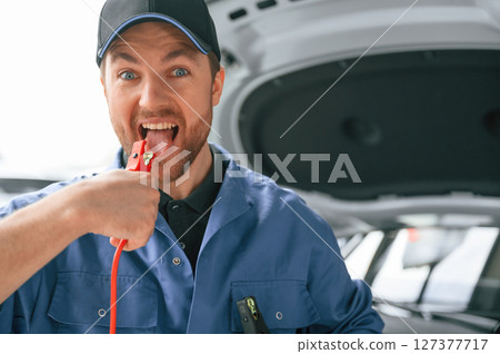 Having fun with electrical terminals, dangerous. Man in blue uniform is working in the car service Having fun with electrical terminals, dangerous. Man in blue uniform is working in the car service 127377717