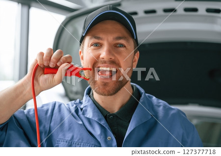 Having fun with electrical terminals, dangerous. Man in blue uniform is working in the car service Having fun with electrical terminals, dangerous. Man in blue uniform is working in the car service 127377718