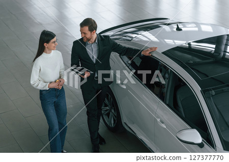 Top view. Man is showing the new automobile to the woman customer in the car dealership 127377770
