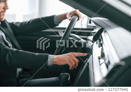 Turning the knobs. Man in formal business clothes is sitting in the modern automobile Turning the knobs. Man in formal business clothes is sitting in the modern automobile 127377940