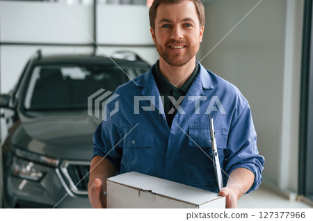 Holding the document, notepad. Man in blue uniform is working in the car service 127377966