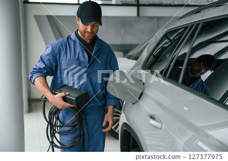 Device with many wires. Fuel system test. Man in blue uniform is working in the car service Device with many wires. Fuel system test. Man in blue uniform is working in the car service 127377975
