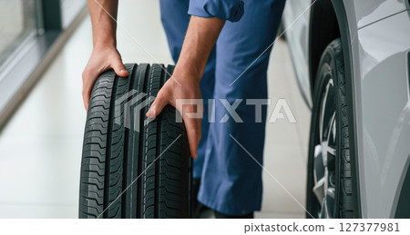 Front view, moving the tire. Man in blue uniform is working in the car service Front view, moving the tire. Man in blue uniform is working in the car service 127377981