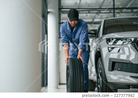 Front view, moving the tire. Man in blue uniform is working in the car service 127377982