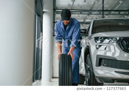 Front view, moving the tire. Man in blue uniform is working in the car service 127377983