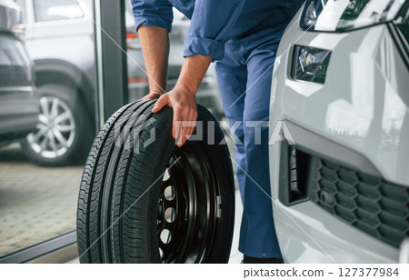 Front view, moving the tire. Man in blue uniform is working in the car service Front view, moving the tire. Man in blue uniform is working in the car service 127377984