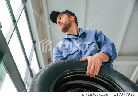View from below. Holding tire. Man in blue uniform is working in the car service View from below. Holding tire. Man in blue uniform is working in the car service 127377986