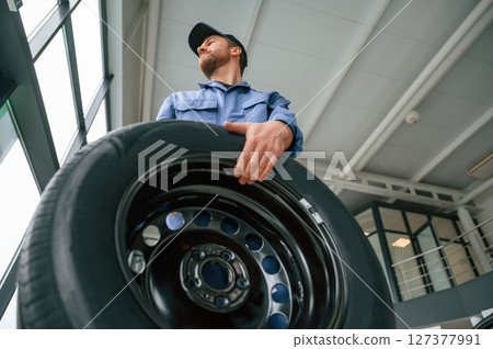 With big new tire for a change. Man in blue uniform is working in the car service 127377991