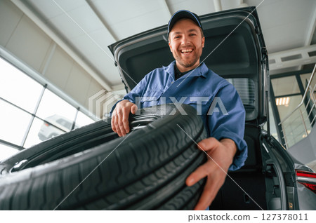 Putting the tire out of automobile. Man in blue uniform is working in the car service 127378011