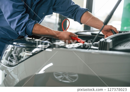 Testing breakage by using electrical terminals. Man in blue uniform is working in the car service 127378023
