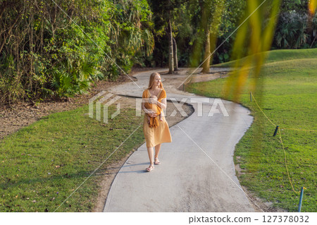 Mother holding her little baby in a yellow sling in the park. Warm and loving family moment. Babywearing, parenting, and mother-child bonding concept Mother holding her little baby in a yellow sling in the park. Warm and loving family moment. Babywearing, parenting, and mother-child bonding concept 127378032