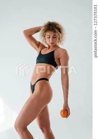 Holding orange fruit. Young caucasian woman with athletic body shape is indoors at daytime Holding orange fruit. Young caucasian woman with athletic body shape is indoors at daytime 127378101