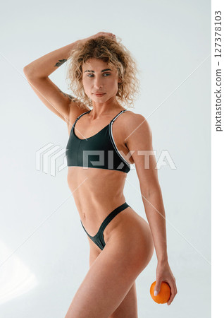 Concept of healthy eating, with orange in hand. Young caucasian woman with athletic body shape is indoors at daytime 127378103