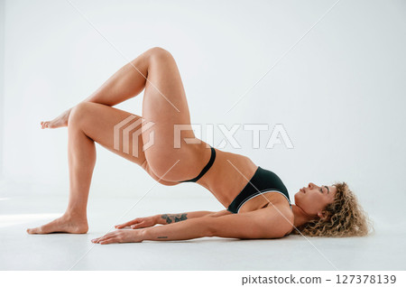 Side view. Lying down on the floor. Young caucasian woman with athletic body shape is indoors at daytime 127378139