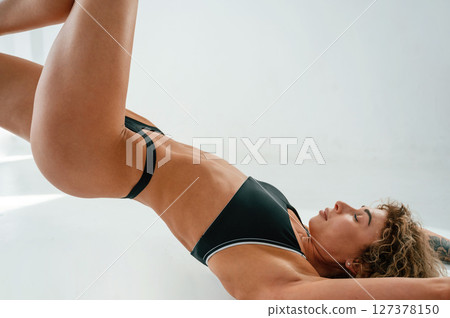 Legs are up. Lying down on the floor. Young caucasian woman with athletic body shape is indoors at daytime 127378150