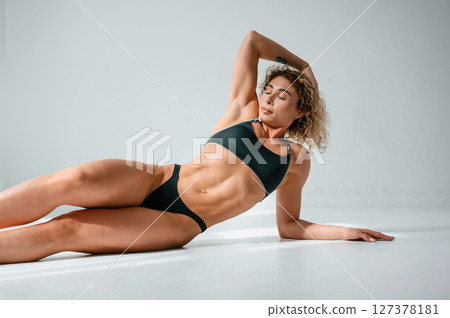 In sportive underwear. On the floor. Young caucasian woman with athletic body shape is indoors at daytime In sportive underwear. On the floor. Young caucasian woman with athletic body shape is indoors at daytime 127378181