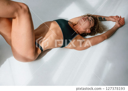 On the floor, beautiful shadows, lying down. Young caucasian woman with athletic body shape is indoors at daytime On the floor, beautiful shadows, lying down. Young caucasian woman with athletic body shape is indoors at daytime 127378193